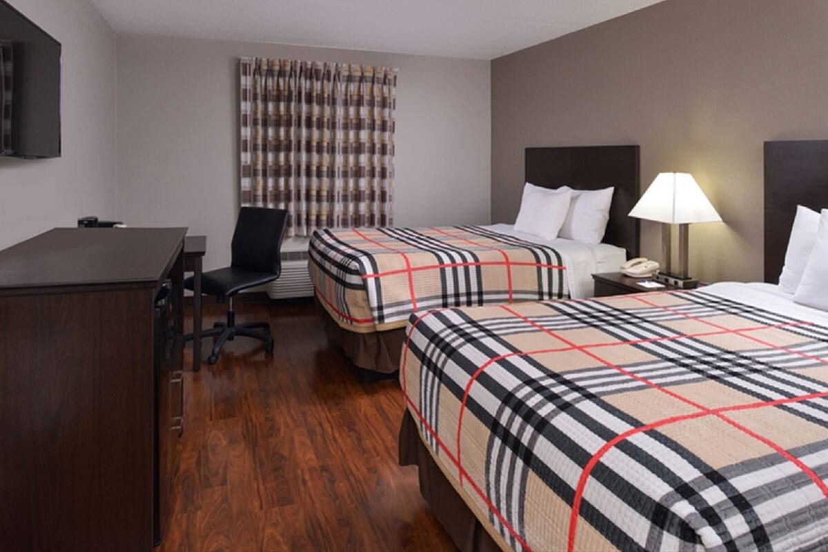 A hotel room with two beds, a desk, a chair, a TV, and a window with curtains.