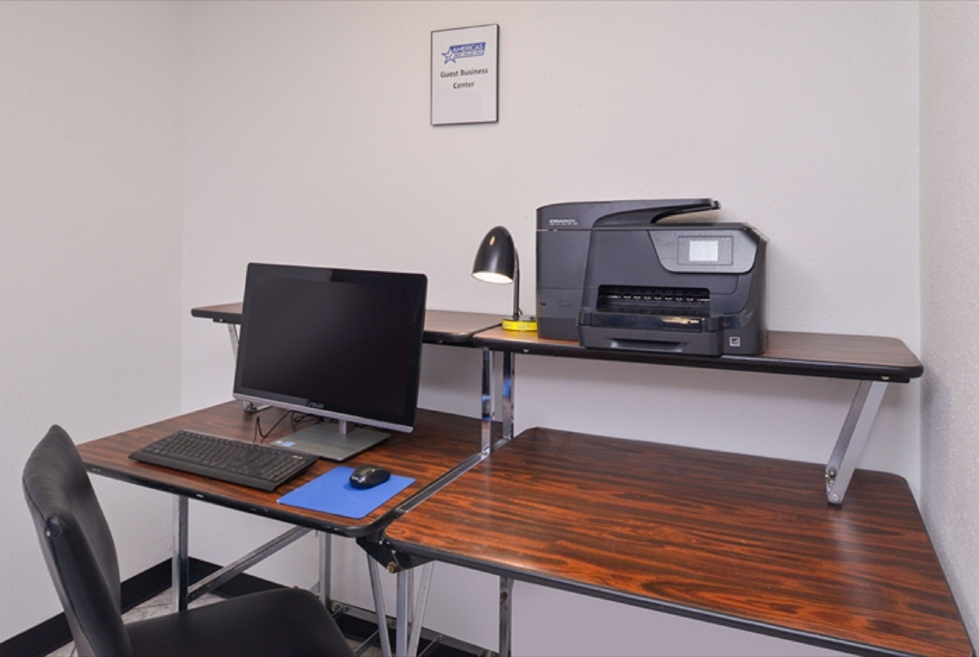 Een bureau met een laptop, een desktopcomputer, een printer, een bureaulamp en een stoel.
