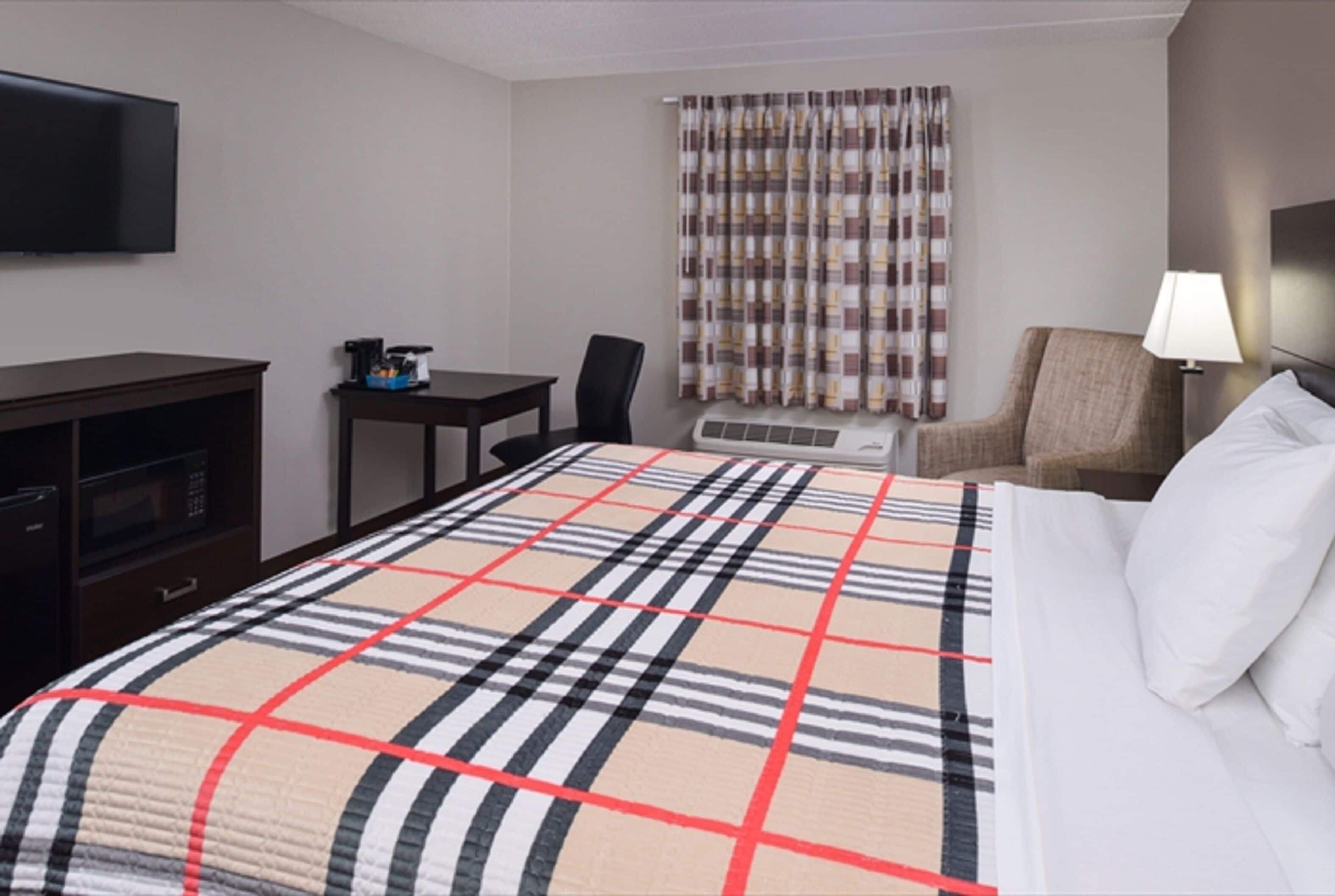 A hotel room with a bed, a TV, a desk, a chair, and a lamp.