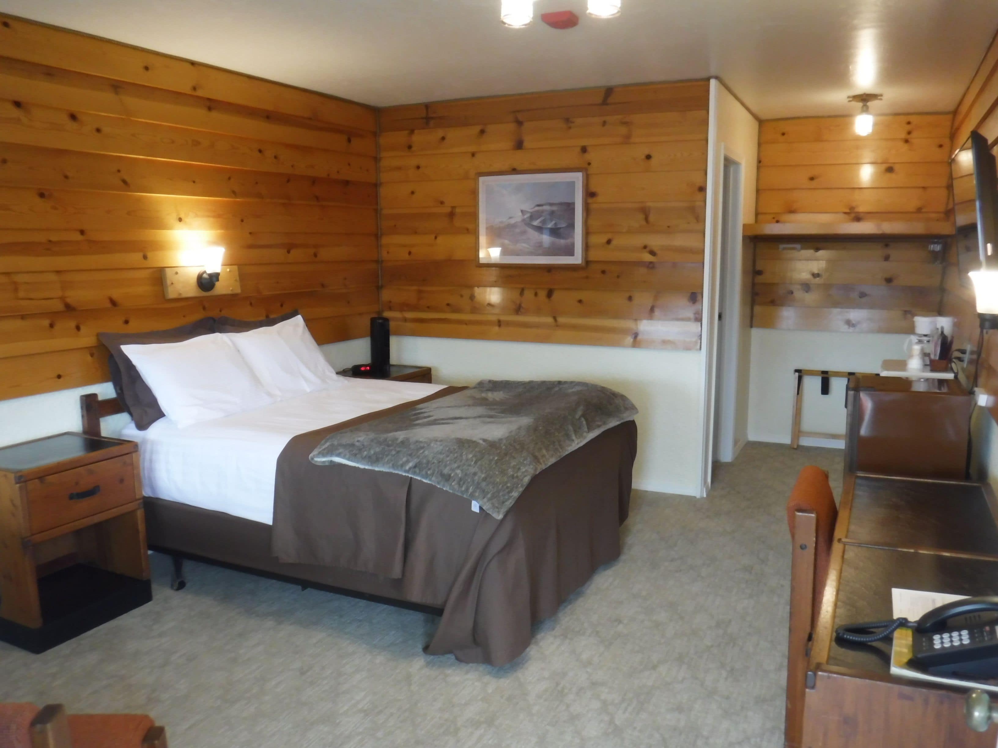 A wooden-paneled bedroom with a bed, bedside table, and a desk with a telephone.