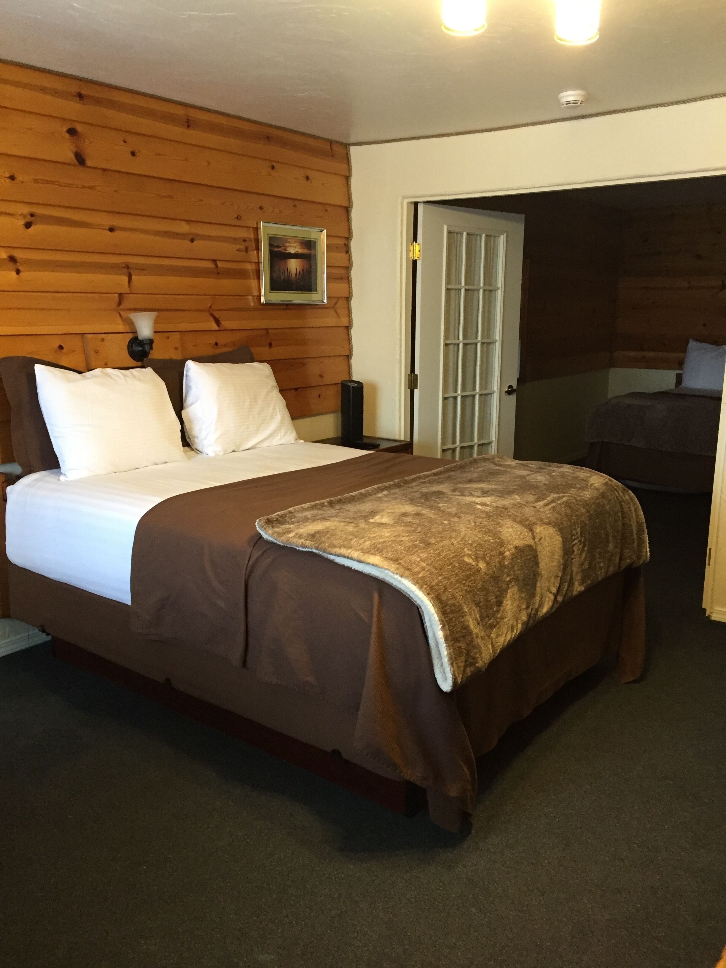 A bedroom with a wooden wall, a bed with white and brown bedding, a bedside table, and a picture on the wall.