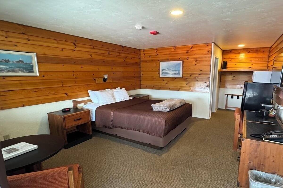 A room with a bed, a desk, a chair, a small table, and a trash bin.