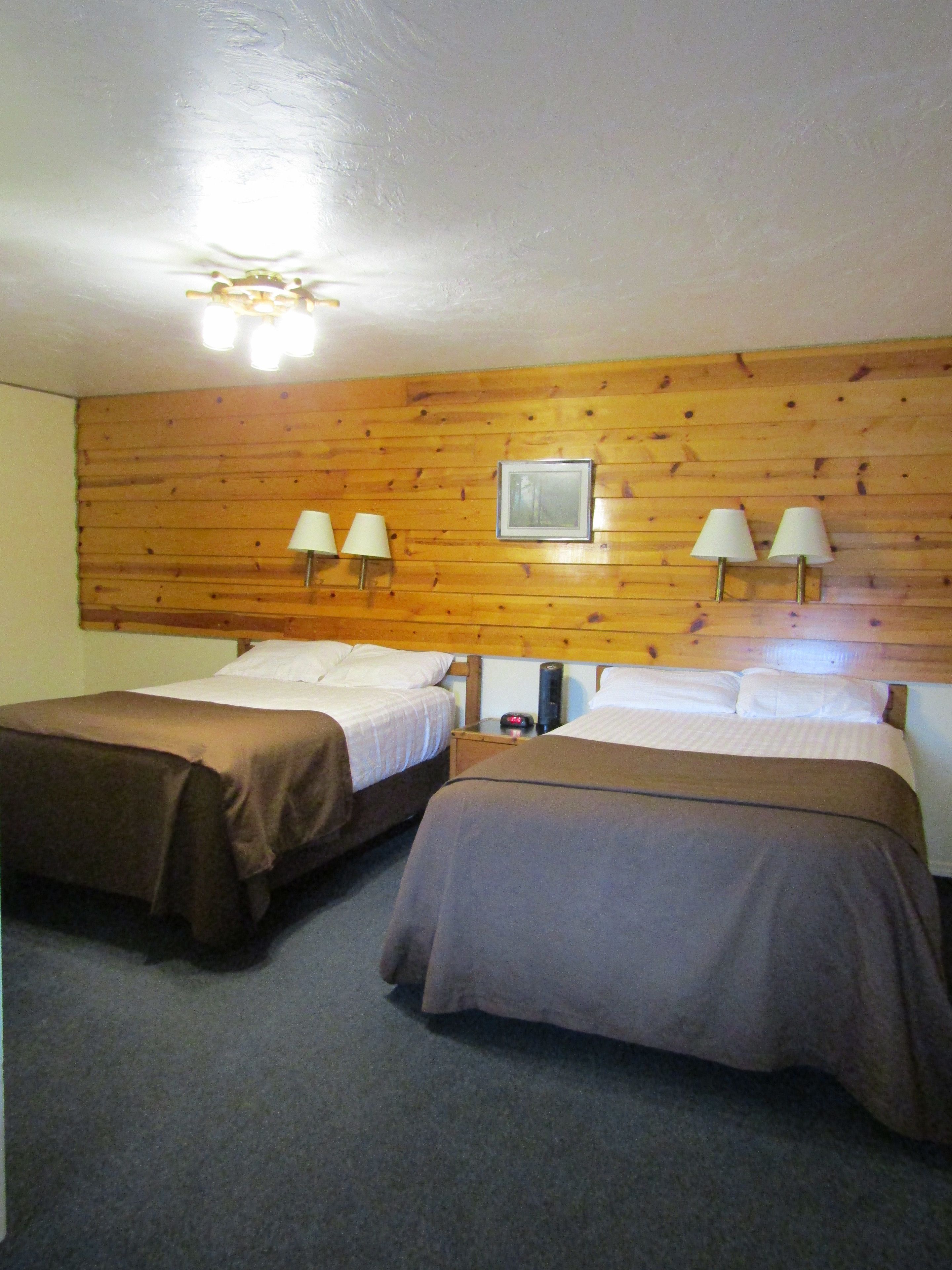 Habitación con dos camas, paredes de paneles de madera y dos lámparas de pared.