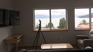 Une pièce comprenant un télescope sur un trépied, un téléviseur fixé au mur, un bureau en bois, un banc et une vue sur un lac avec des montagnes à l’horizon.