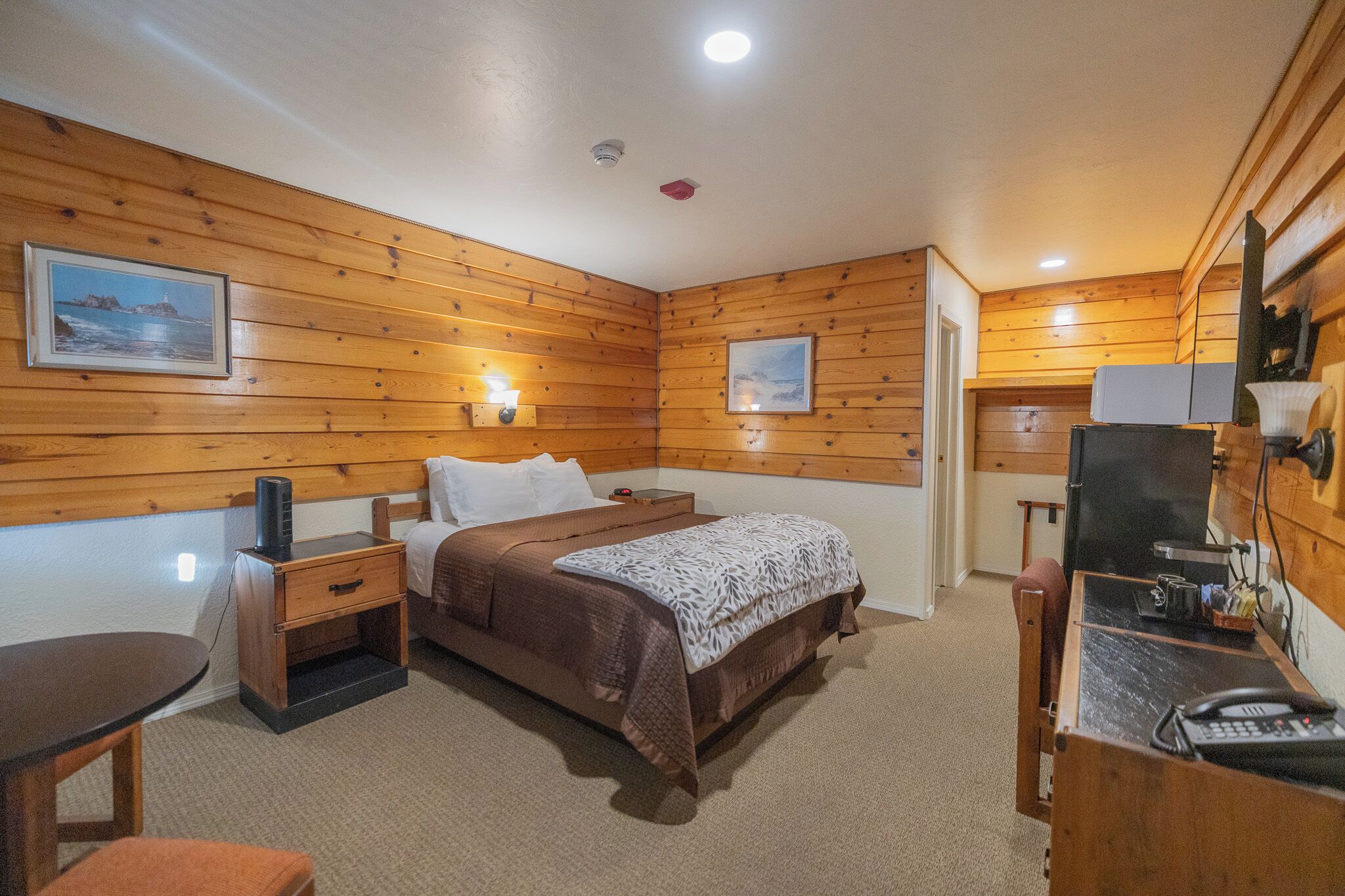 A wooden-paneled room with a bed, bedside table, desk, and chair.