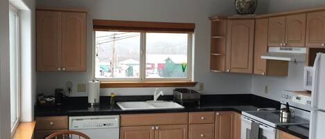 A kitchen with wooden cabinets, a black countertop, a sink, a stove, and a dining table with chairs.