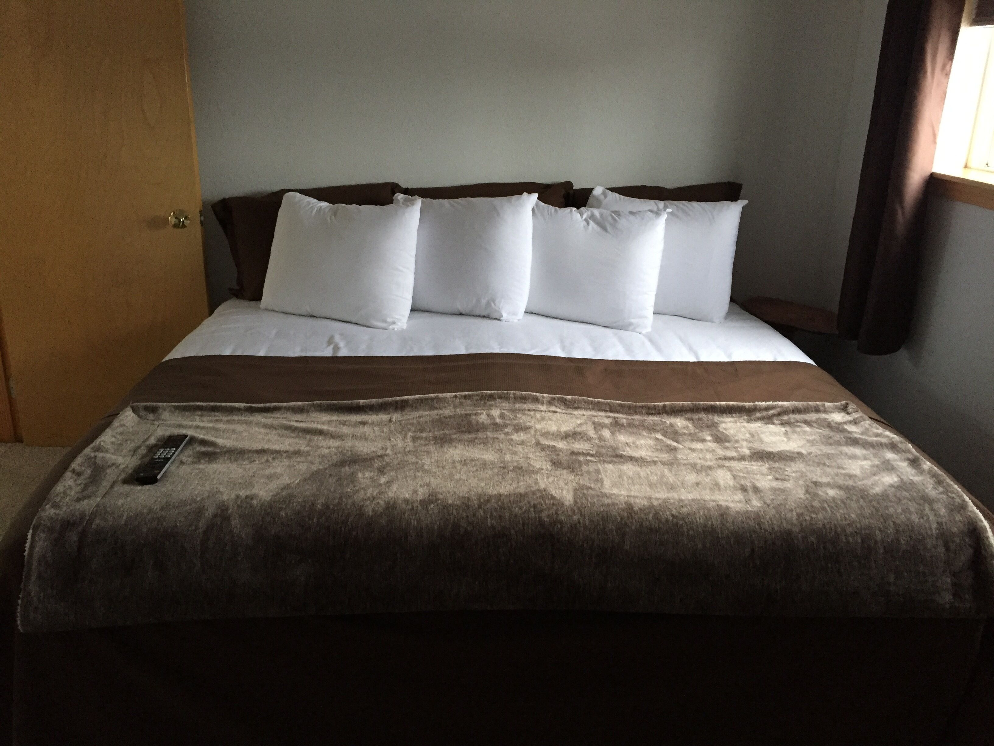 A bed with white bedding and a brown throw blanket.