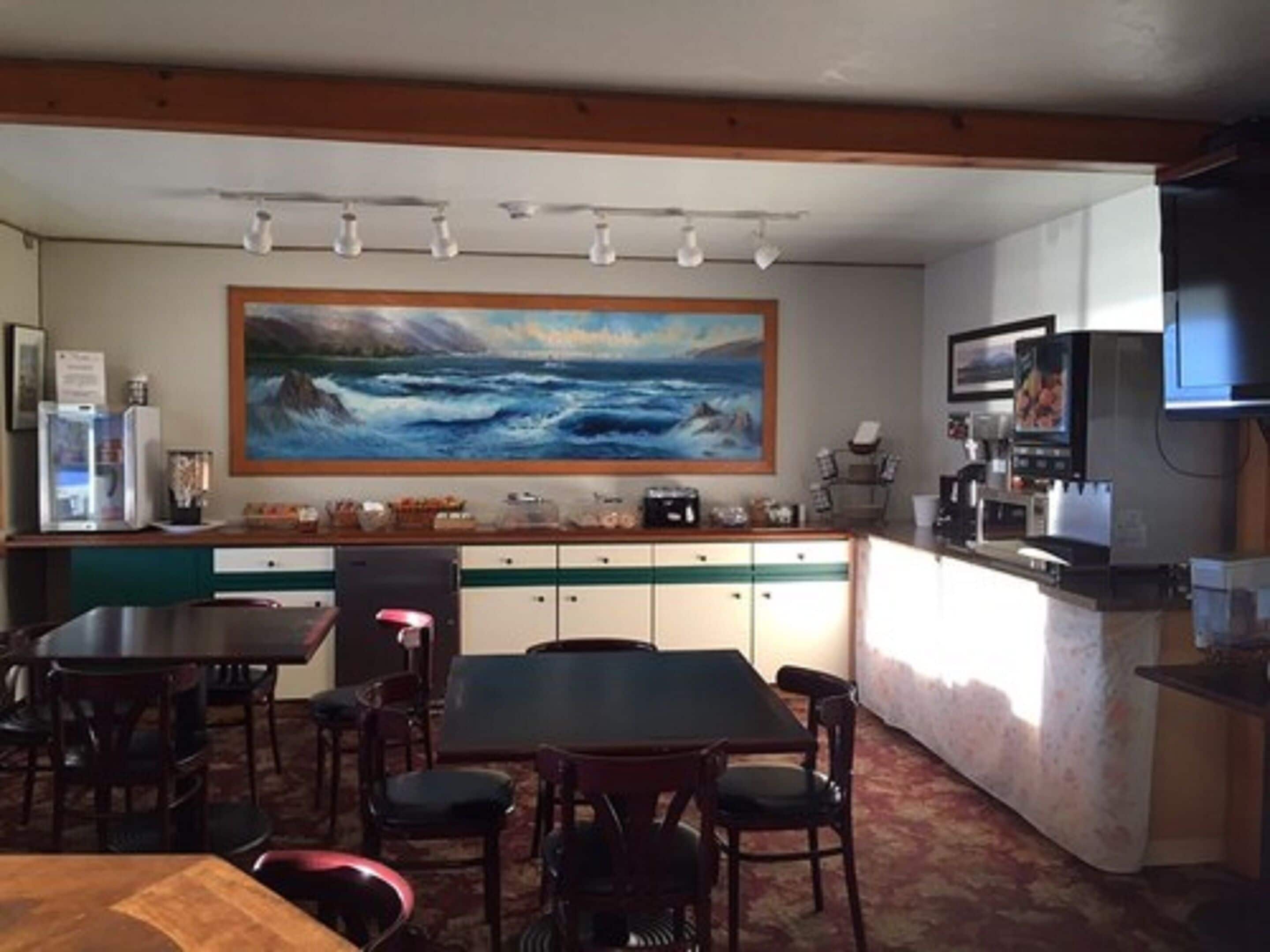 Un comedor con un cuadro grande de una vista marina, una cocina con microondas y un televisor montado en la pared.