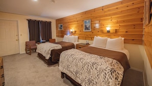 Une chambre d’hôtel avec deux lits, des lambris en bois sur les murs, une porte, une chaise et une petite table.