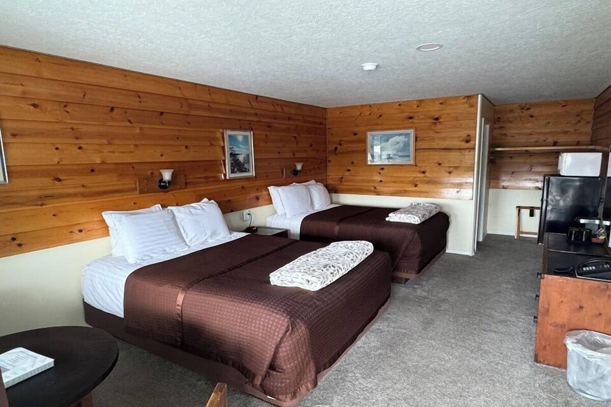 A room with two beds, wooden walls, a small desk with a television, and a trash bin.