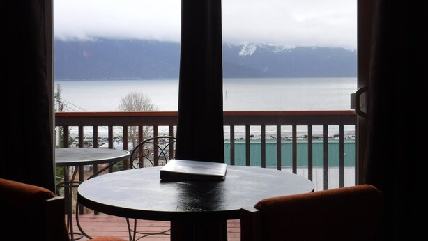 Un balcon avec vue sur un lac et des montagnes, comprenant une table et des chaises.