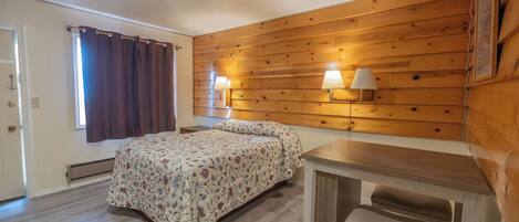 A bedroom with a wooden wall, a bed with floral bedding, two bedside lamps, and a desk with a chair.