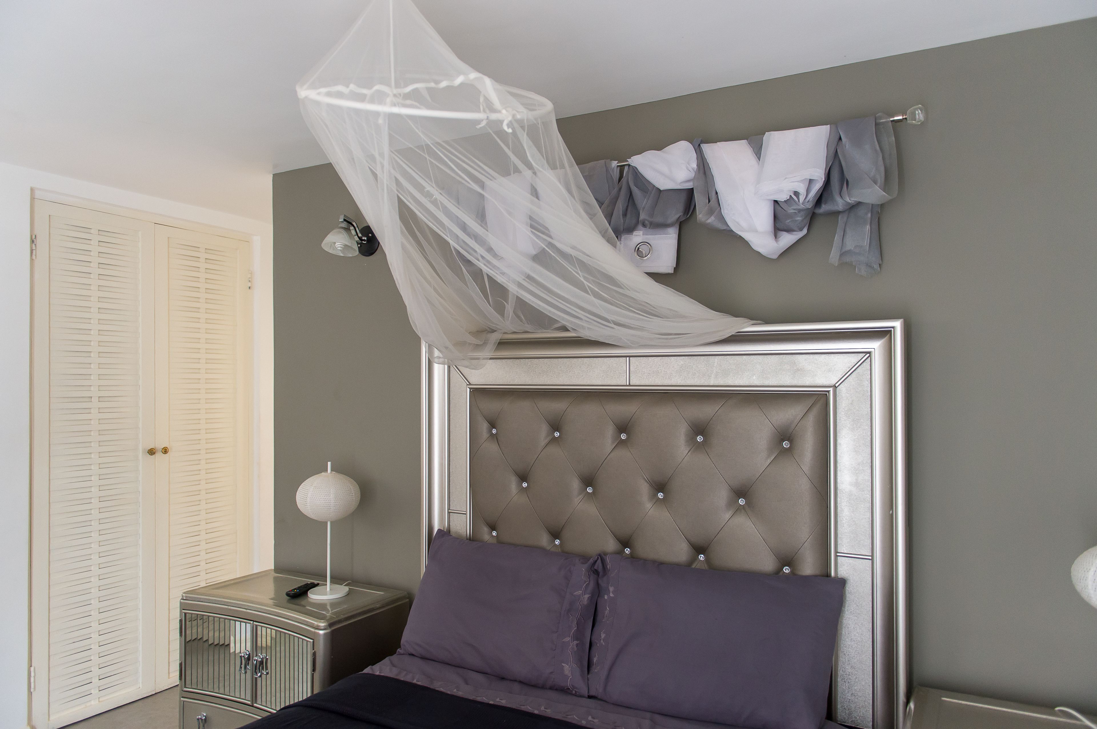 Quarto com cabeceira estofada, mesa de cabeceira com abajur e um cabideiro.