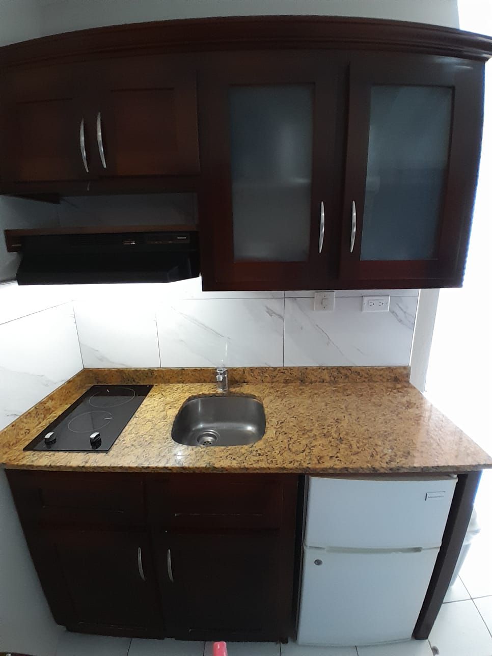 A compact kitchen with dark wooden cabinets, a granite countertop, a stainless steel sink, and a built-in dishwasher.
