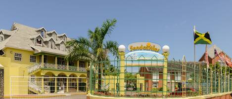 Un hotel con fachada amarilla, un letrero que dice "Sandcastle" y una bandera de Jamaica.