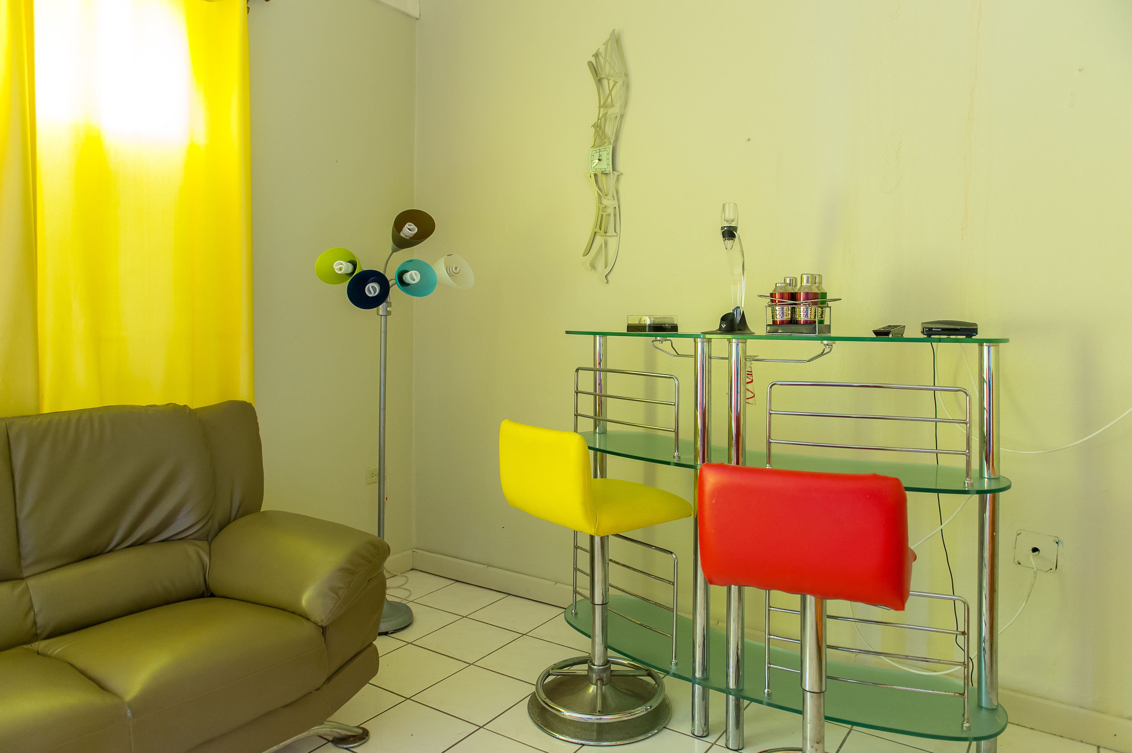 A room with a beige sofa, a glass table with two chairs, and a wall-mounted lamp.