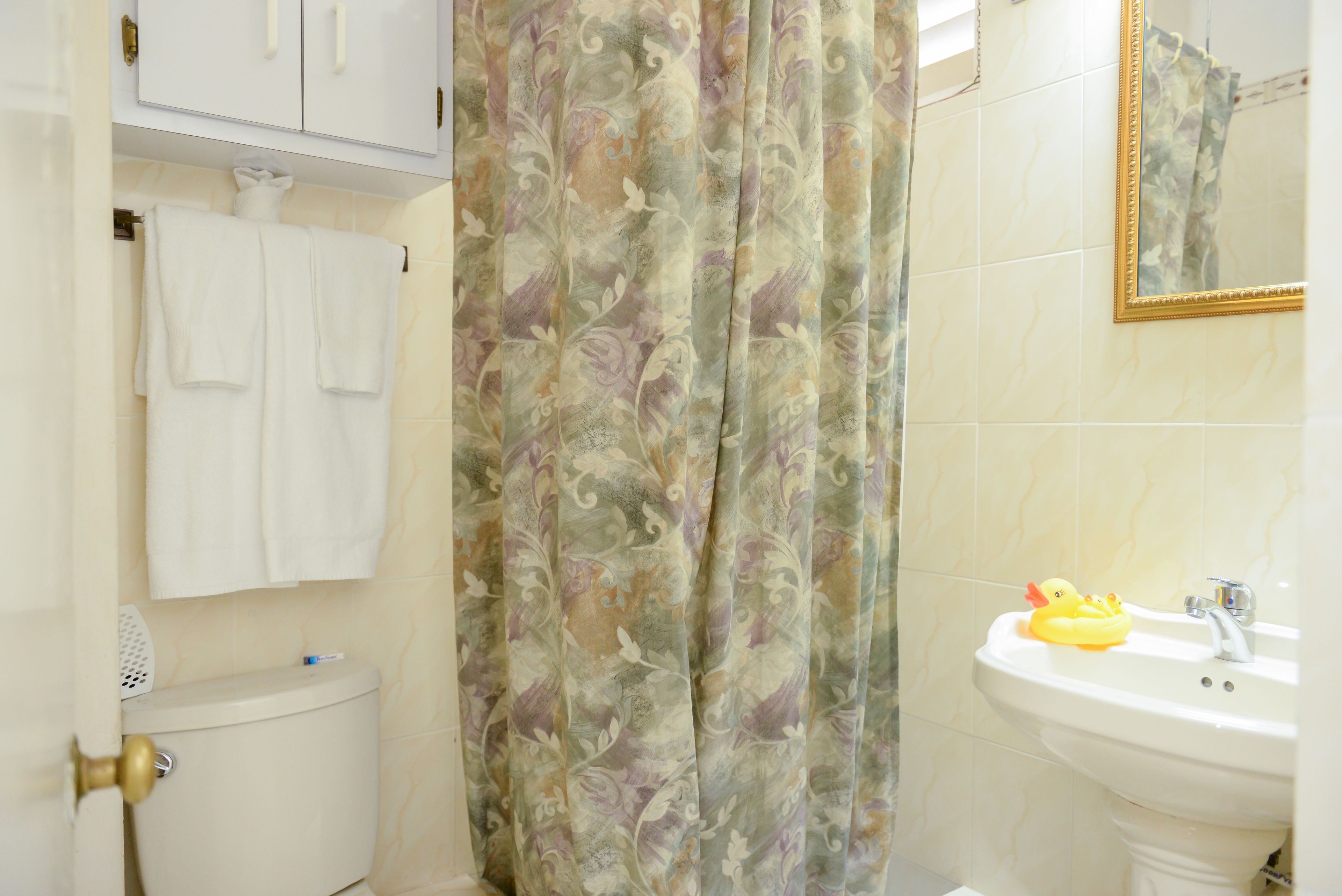 A bathroom with a toilet, a sink, a shower curtain, and a mirror.