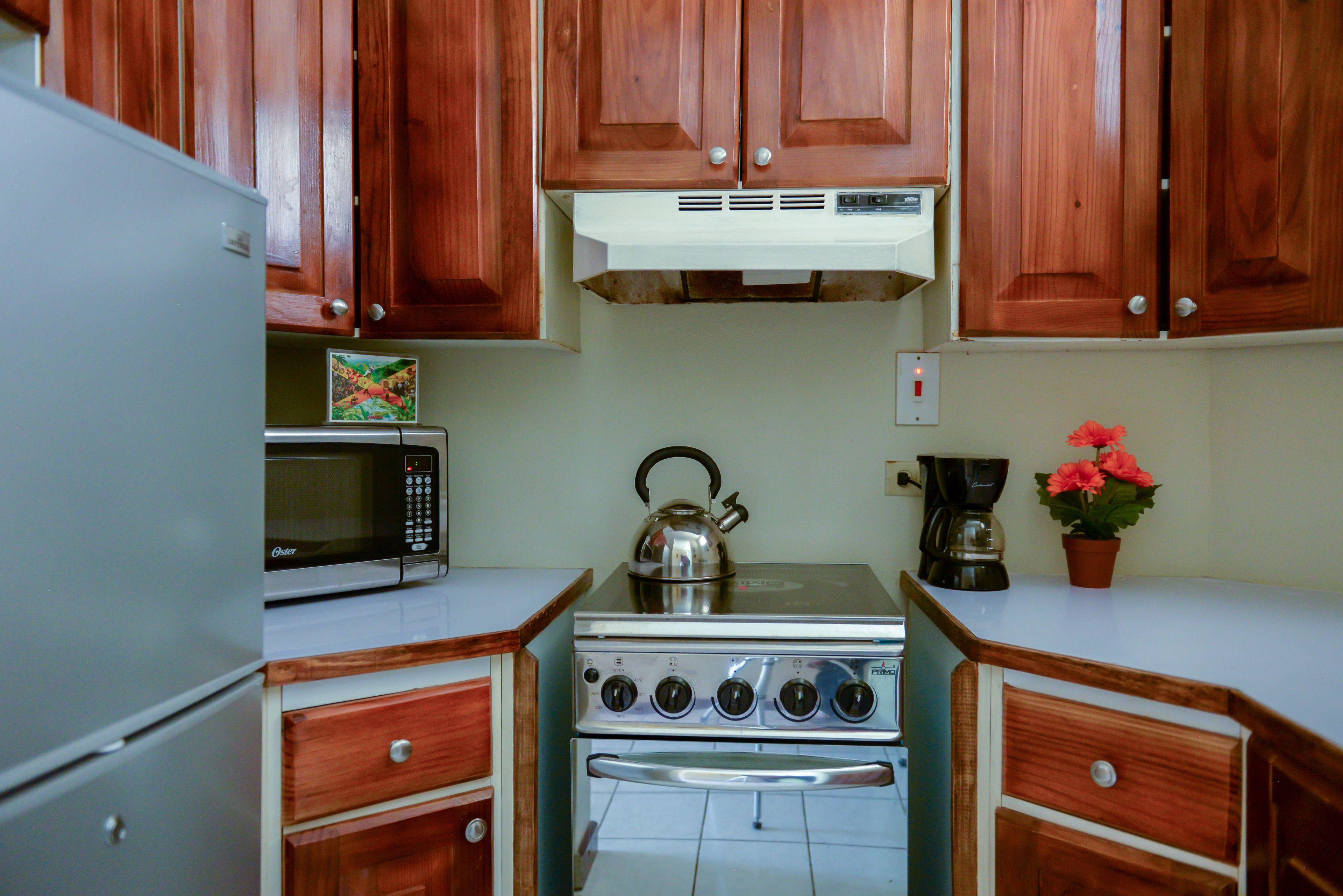 A kitchen with wooden cabinets, a microwave, a kettle, a stove, and a coffee maker.
