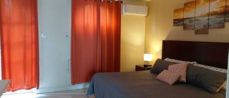 A bedroom with a bed, curtains, a nightstand, a lamp, and a wall with paintings.