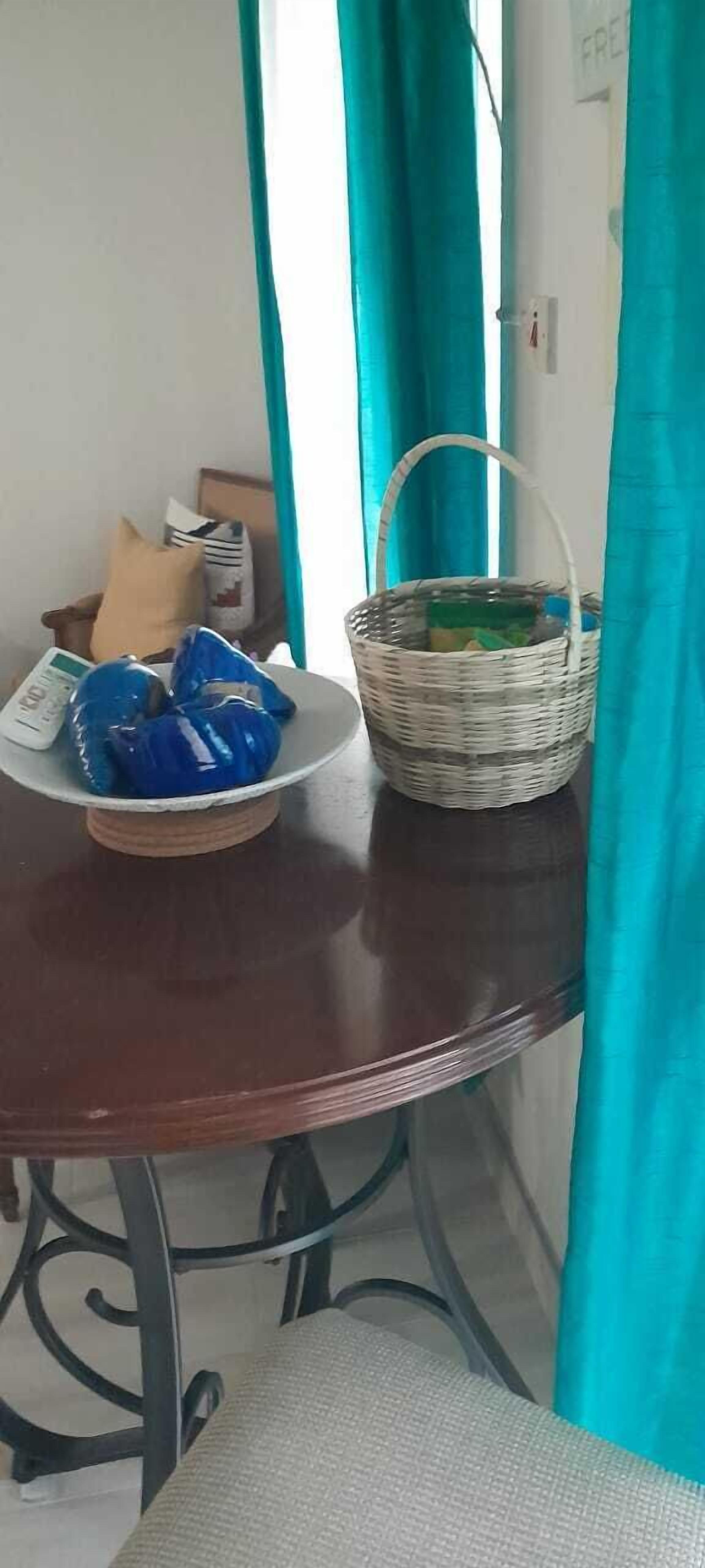 A round wooden table with a woven basket and a plate of blue plastic bags.