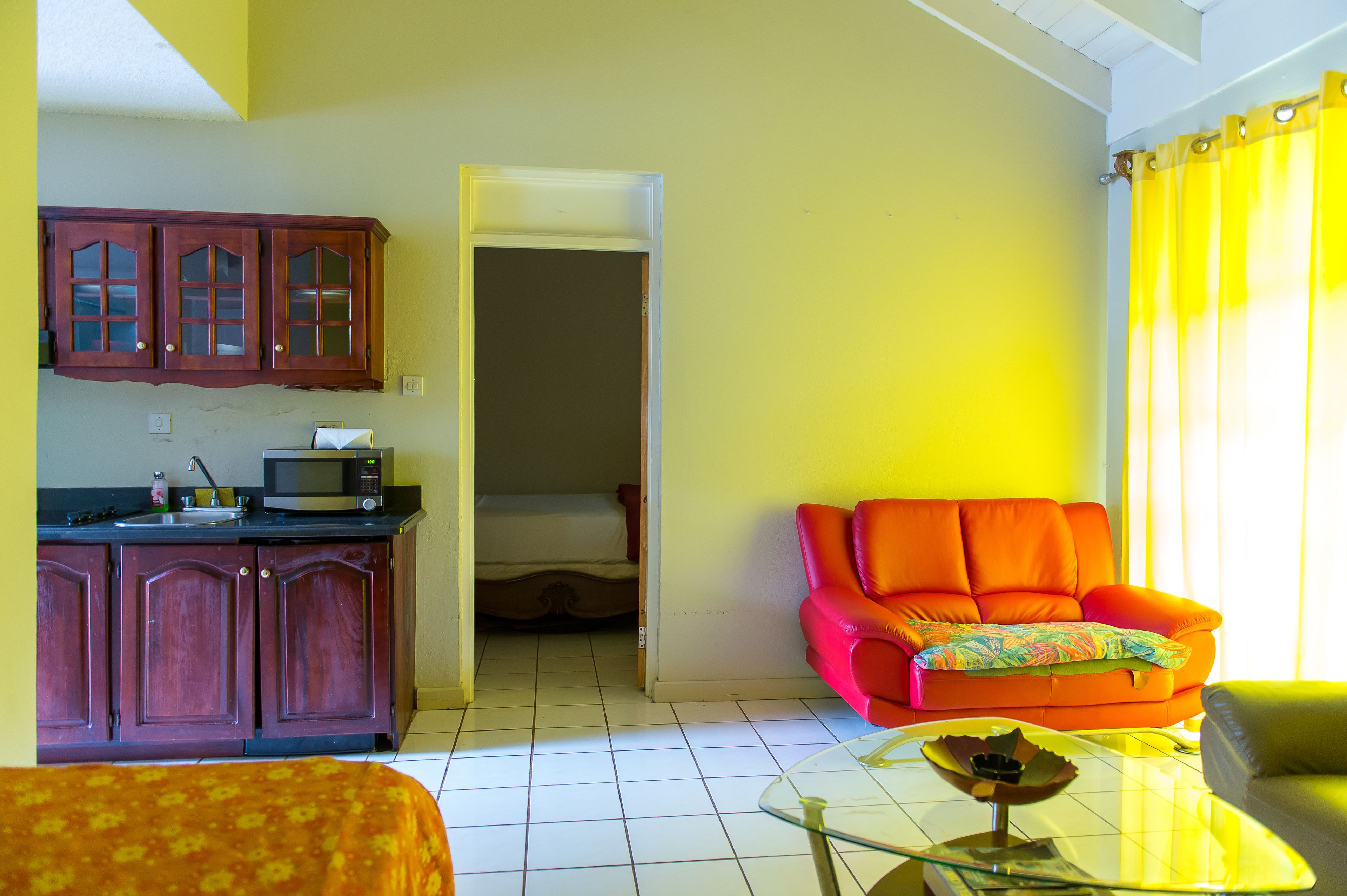 Een kamer met een kitchenette, een bed, een feloranje bank en een glazen salontafel.