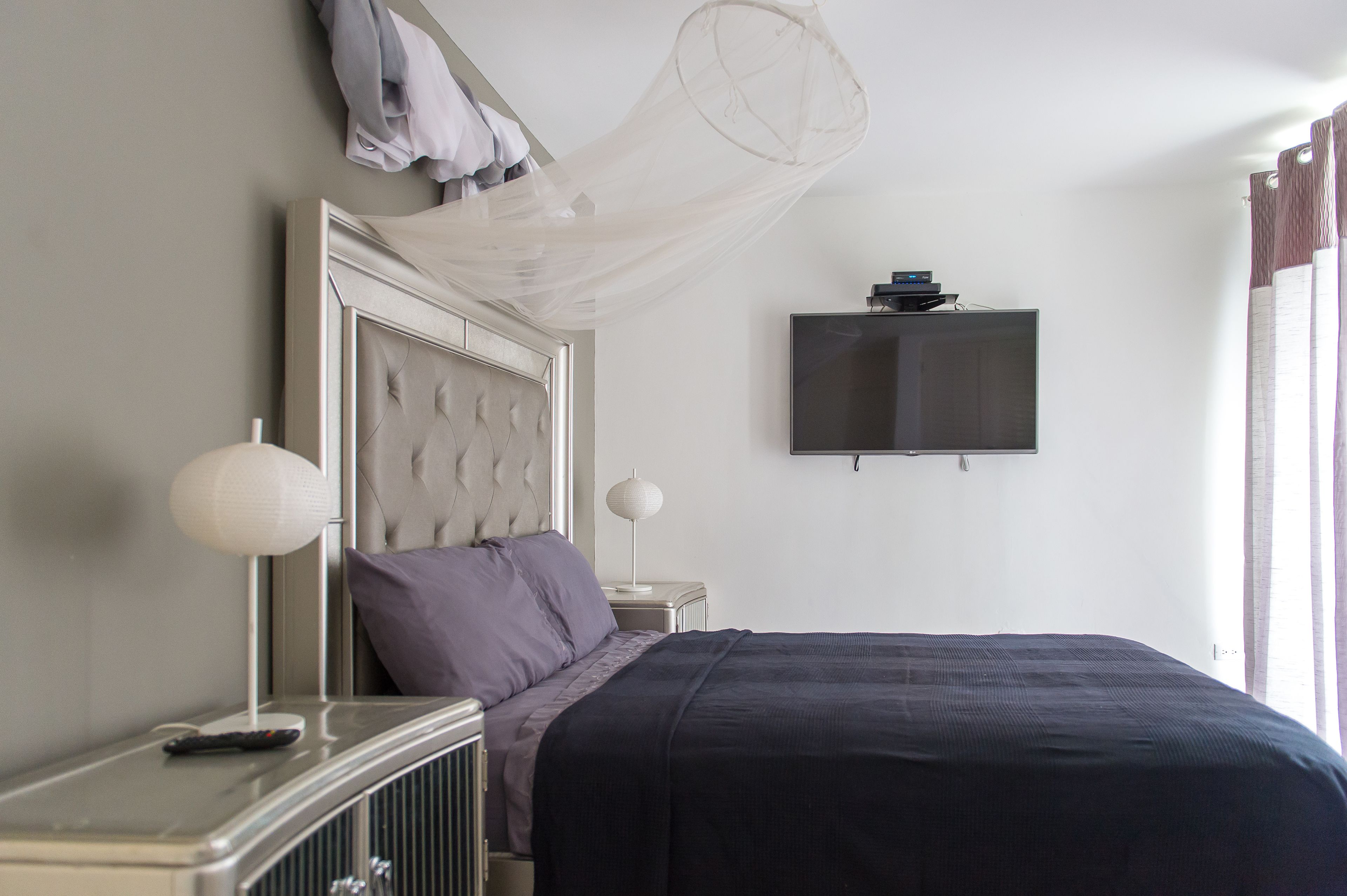 A neatly arranged bedroom with a bed, bedside tables, a television, and a hanging mosquito net.