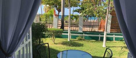 A patio with a glass table and two chairs, surrounded by a white fence and palm trees.
