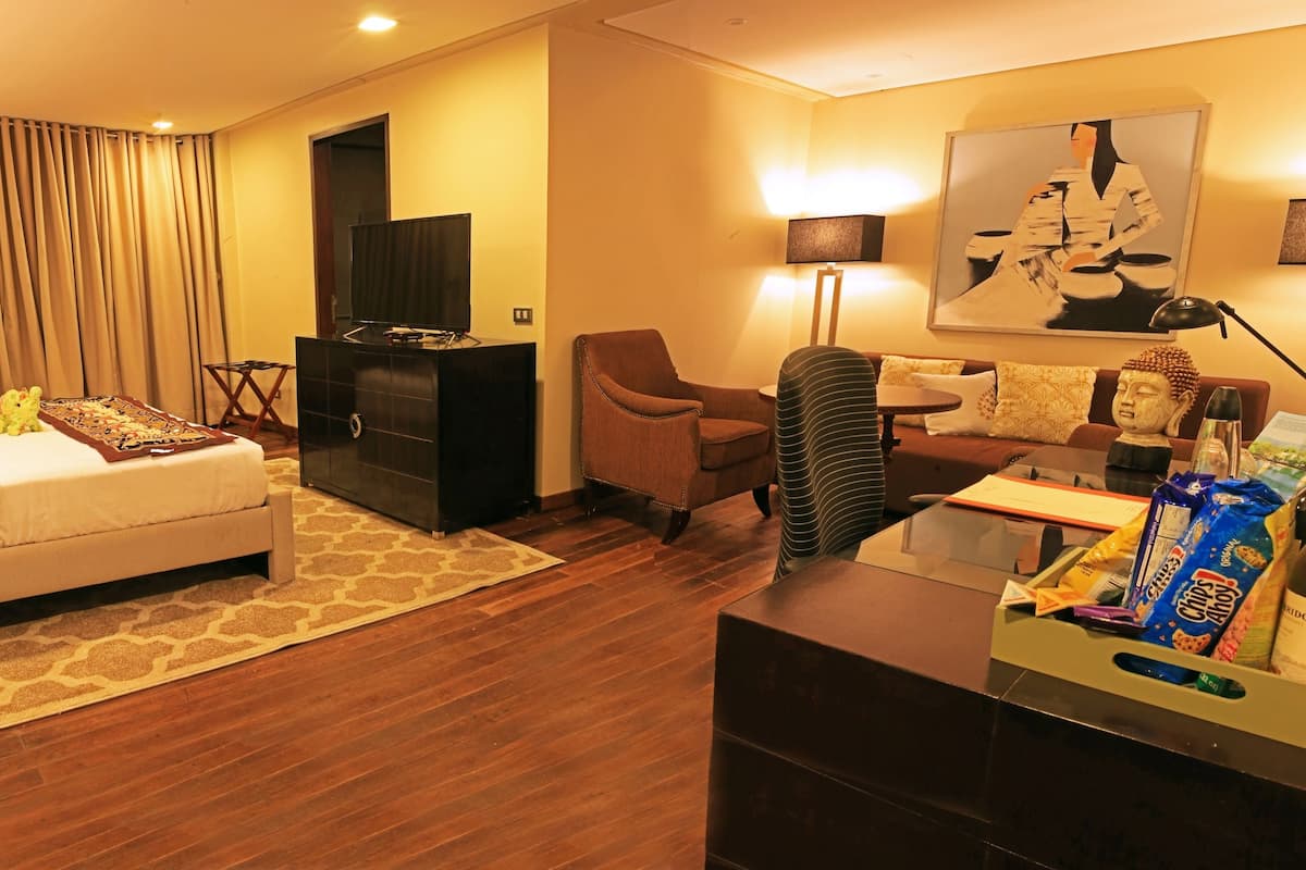 A hotel room with a bed, a desk, a chair, a sofa, a television, and a Buddha statue.