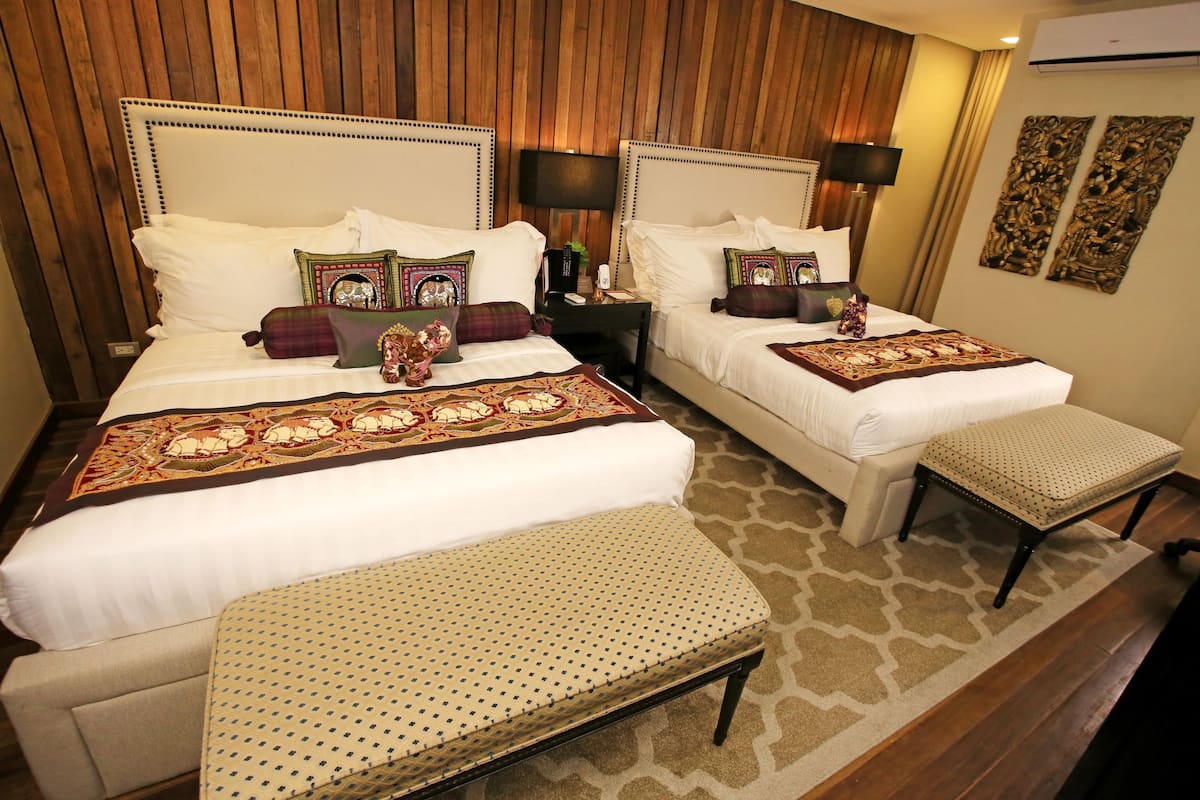 A hotel room with two beds, a bench, and a nightstand with a lamp.