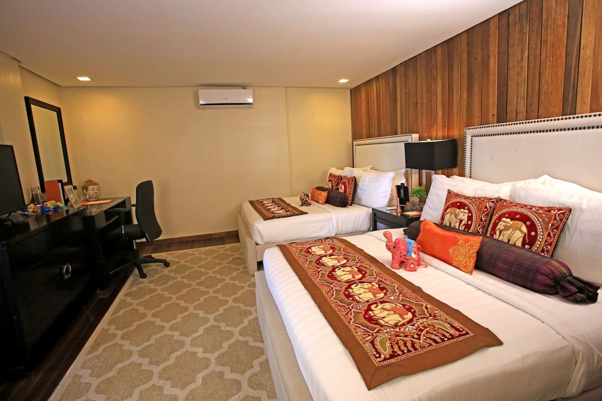 A hotel room with a large bed, two smaller beds, a desk, and a chair.