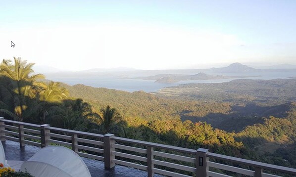 Une vue panoramique depuis un balcon donnant sur un paysage côtier, avec des palmiers et une étendue d’eau au loin.