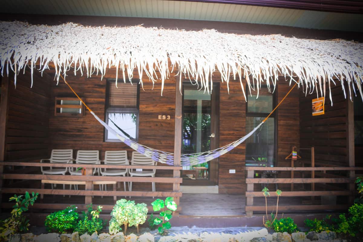 Une cabane en bois avec un toit de chaume, un hamac et des sièges d’extérieur.