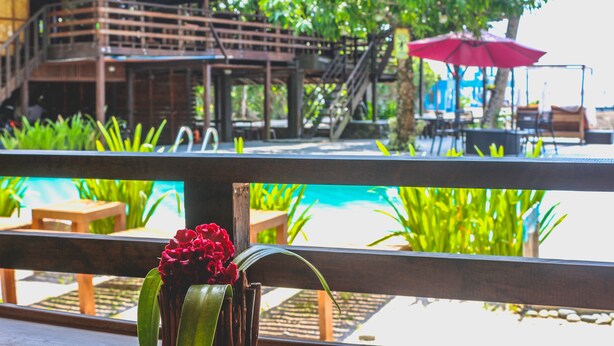 A wooden deck with a pool and outdoor seating, overlooking a building with a staircase. - Seasta Beach Resort (Baler)