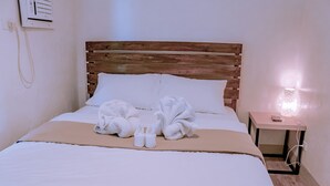 A neatly made bed with white linens, a wooden headboard, and a bedside table with a lamp and a remote control. - Seasta Beach Resort (Baler)