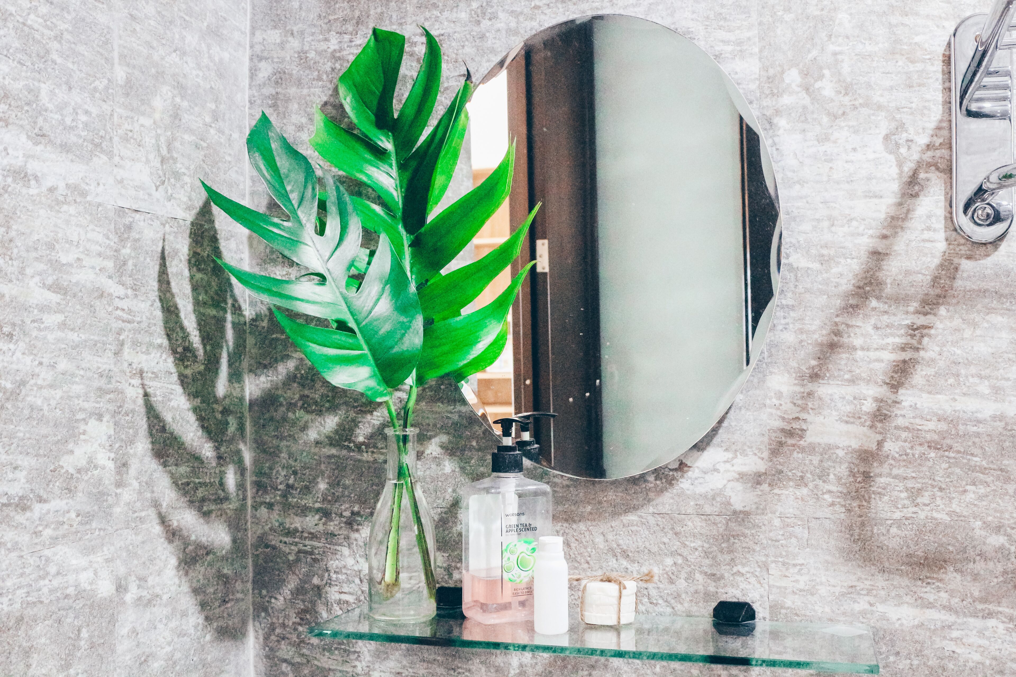A bathroom with a marble wall, a glass shelf with toiletries, and a large mirror.
