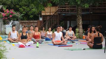 A group of people sitting on yoga mats outdoors, with trees and a wooden structure in the background.