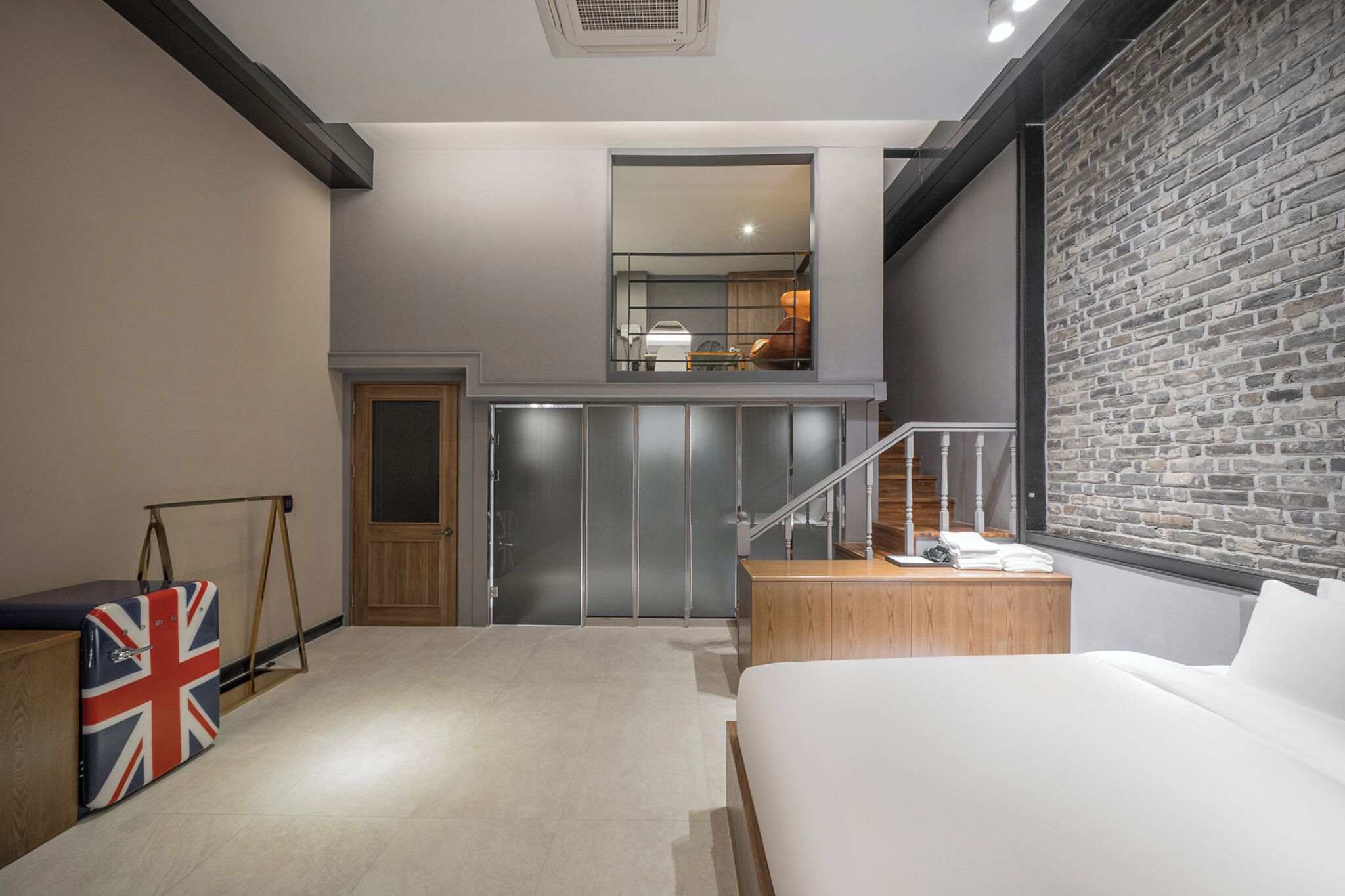 Un dormitorio moderno con cama, un escritorio pequeño, un espejo y una escalera que sube a un nivel superior.