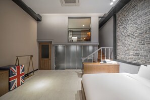 A modern bedroom with a bed, a small desk, a mirror, and a staircase leading to an upper level. - ACT Hotel Urban (Daegu)