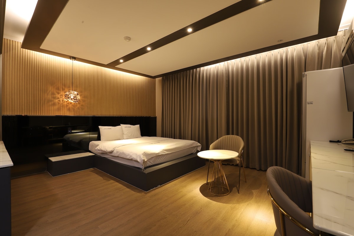 Quarto de hotel moderno com cama, mesa de cabeceira, cadeira e televisão.