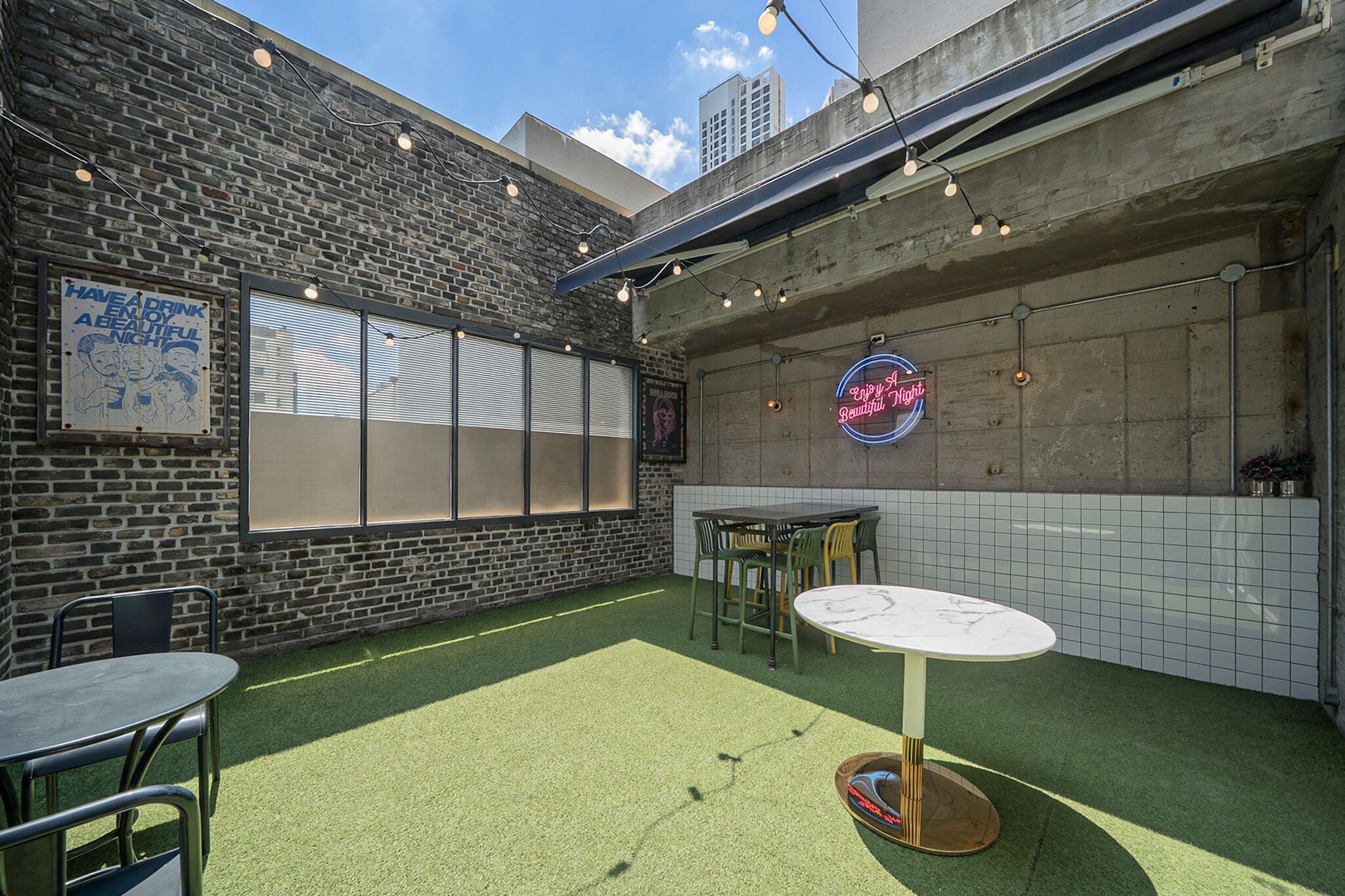 Un patio al aire libre con pared de ladrillo, un letrero de neón y una mesa con sillas.