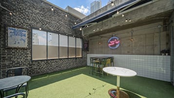 Un patio al aire libre con pared de ladrillo, un letrero de neón y una mesa con sillas.