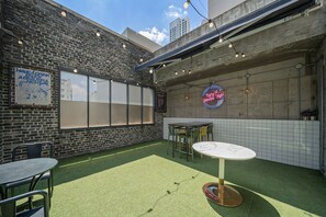An outdoor patio area with a brick wall, a neon sign, and a table with chairs. - ACT Hotel Urban (Daegu)