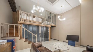 A spacious living area with a high ceiling, a staircase leading to an upper level, a leather sofa, a marble coffee table, and a flat-screen TV. - ACT호텔 어반 (Daegu)