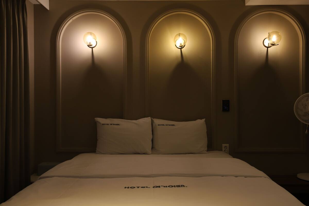 A hotel room with a bed, two pillows, and three wall-mounted light fixtures.