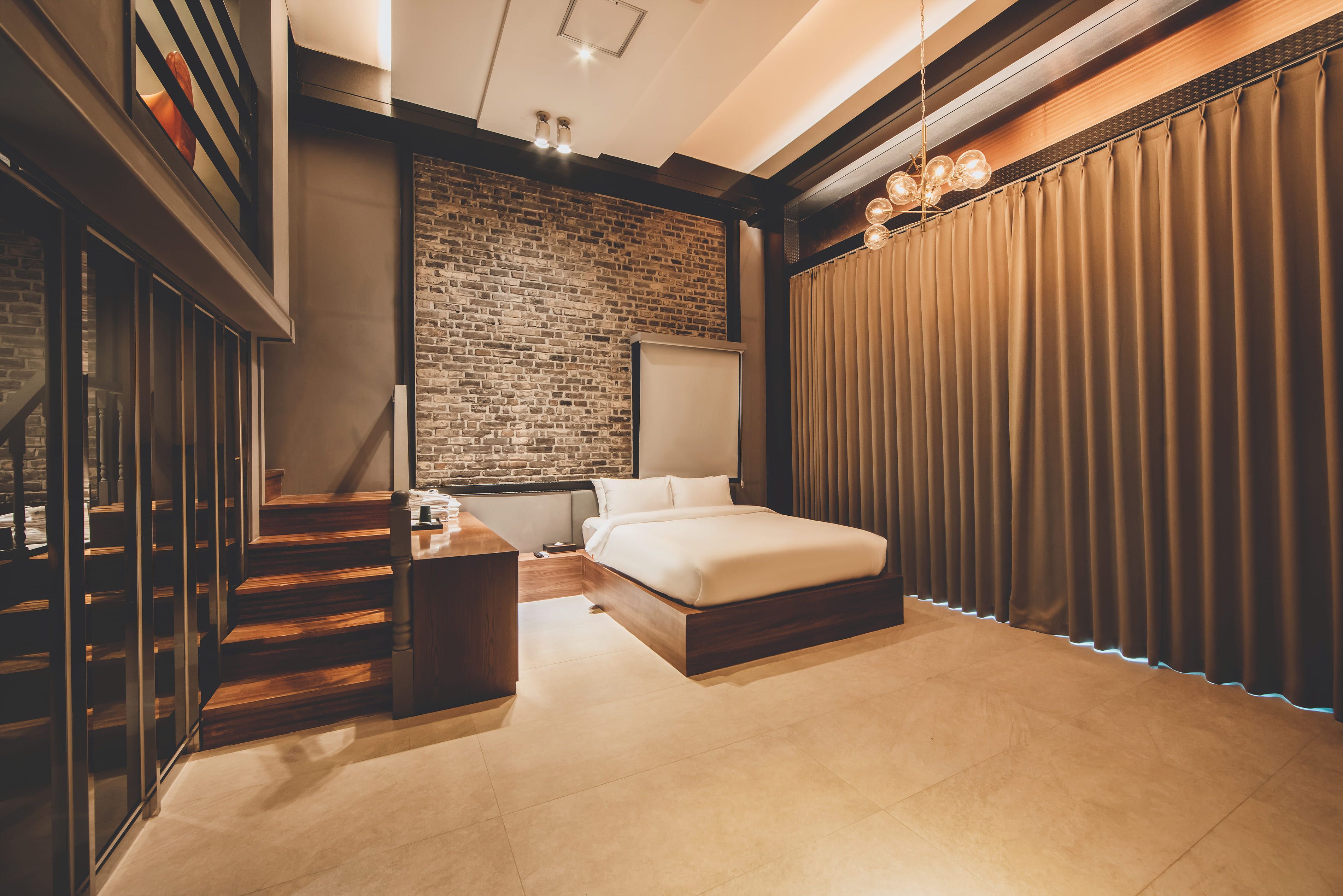 Ein modernes Schlafzimmer mit Backsteinwand, einem großen Bett, einer Holztreppe und Blick ins Freie.