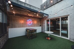 An outdoor patio with a table and chairs, string lights, and a neon sign.