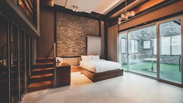 A modern bedroom with a brick wall, a large bed, a wooden staircase, and a sliding glass door leading to an outdoor area.
