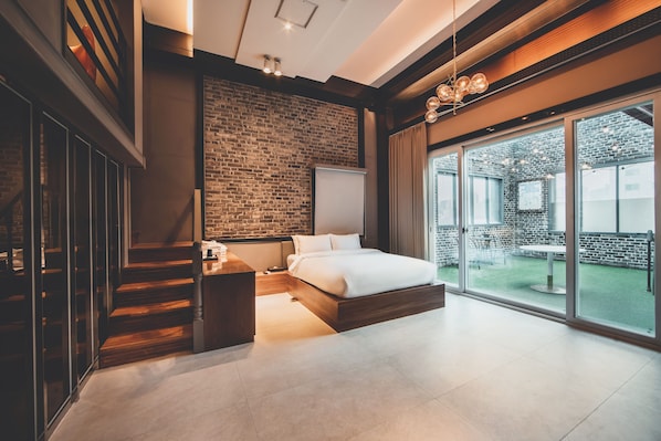 Un dormitorio moderno con pared de ladrillo, una cama grande, una escalera de madera y un ventanal corredero que da a un área exterior.