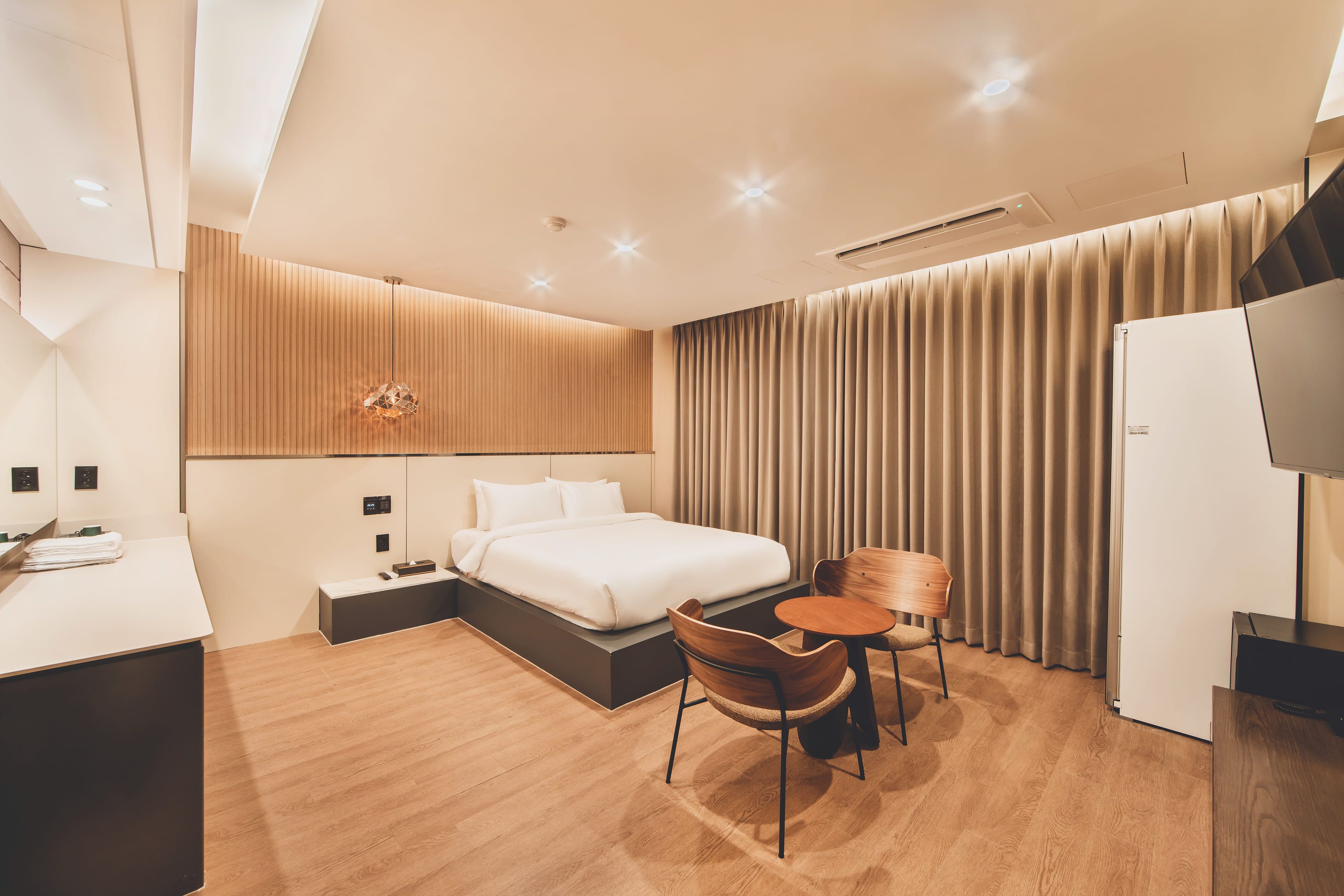 A modern hotel room with a bed, a desk, a chair, a TV, and a curtain.