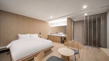 A modern hotel room with a large bed, a small desk, a chair, and a shower area.